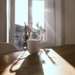 Steaming mug on a wooden table in front of a sunlit window
