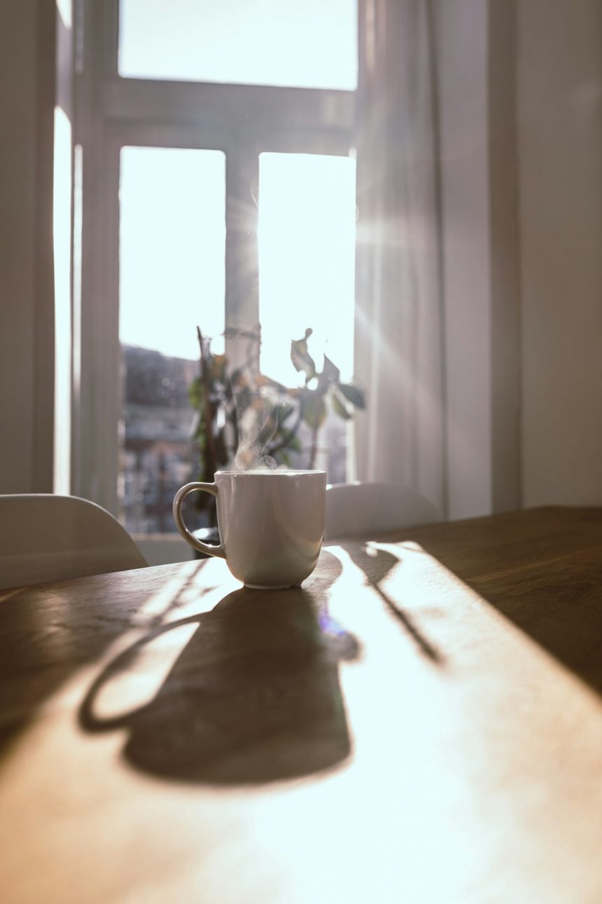Steaming mug on a wooden table in front of a sunlit window