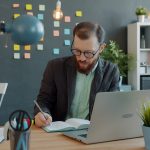 Business owner writing in a notebook beside a laptop at a quiet desk