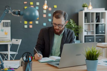 Business owner writing in a notebook beside a laptop at a quiet desk