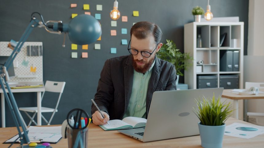Business owner writing in a notebook beside a laptop at a quiet desk
