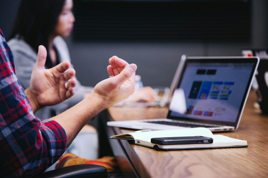 Consultant explaining a proposal to a client across a table with a laptop