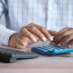 Small business owner using a calculator at a desk with a coffee mug