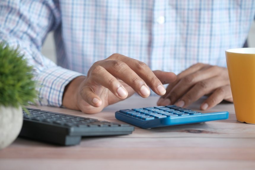 Small business owner using a calculator at a desk with a coffee mug